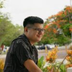 Portrait of a man with glasses smiling in a vibrant park setting in Merida, Yucatan, Mexico.